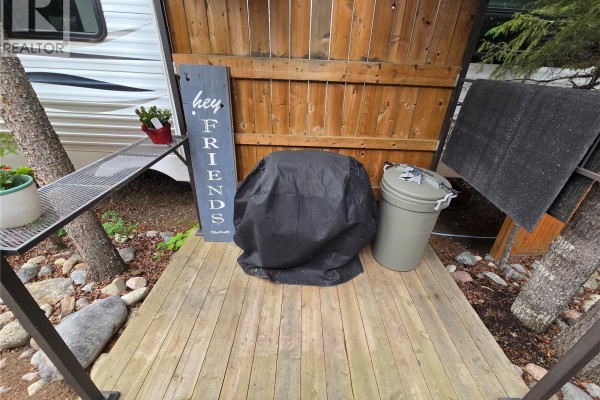 Deck area with a covered grill, trash can, and metal shelving unit. - 320 Fairway Drive, Candle Lake