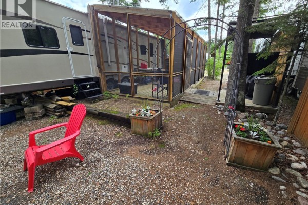 Travel trailer with a screened-in porch extension and a red lawn chair. - 320 Fairway Drive, Candle Lake