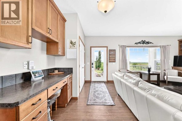 Kitchen island with three dark chairs facing a granite countertop and wooden cabinets. - 320016 402 Avenue E, Rural Foothills County