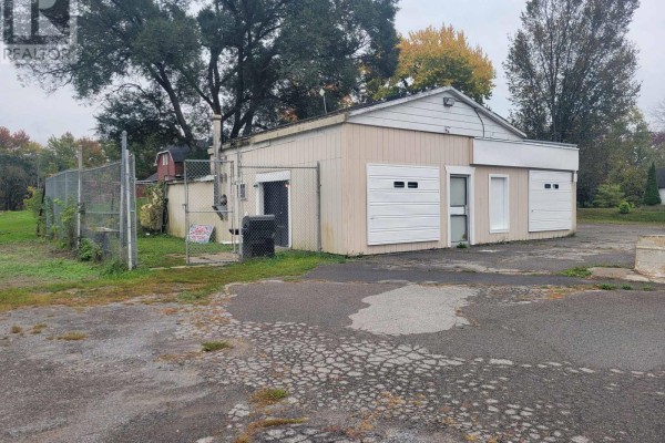 Rear side view of commercial building with chain-link fence and surrounding trees. - 3201 County Road 41, Greater Napanee