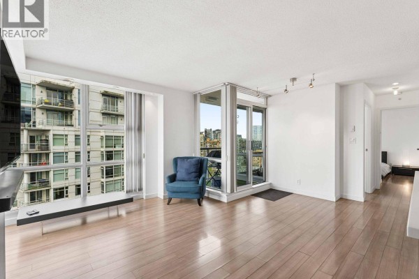 Living area with hardwood floors, blue armchair, and city view through large windows. - 3202 193 Aquarius Mews, Vancouver