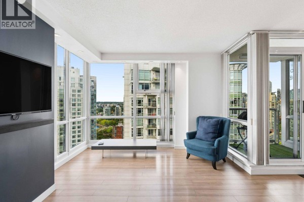 Spacious living room with hardwood floors, blue armchair, and floor-to-ceiling windows. - 3202 193 Aquarius Mews, Vancouver