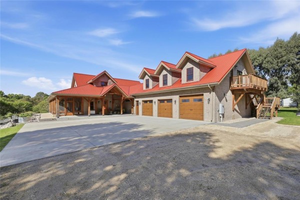 Exterior view of a house with a red metal roof, stucco siding, and a three-car garage. - 32022 Rat River Road, St Pierre Jolys