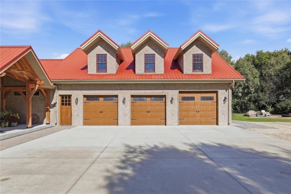 Three-car garage doors with wooden finish and dormer windows on the upper level. - 32022 Rat River Road, St Pierre Jolys