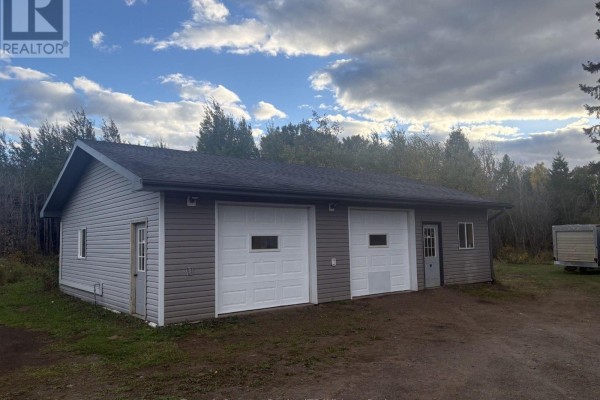 Two-bay detached garage with white doors and grey siding, set on a gravel driveway surrounded by trees. - 3203 Hwy 61 Highway, Thunder Bay Remote Area