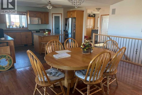 Dining area with a round wooden table and six chairs, adjacent to a kitchen with wooden cabinets. - 32048 Twp Rd 812, Rural Fairview No  136, M D  Of
