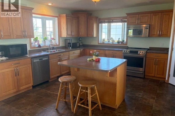 Kitchen with honey oak cabinets, stainless steel appliances, a central island with two stools, and a tiled floor. - 32048 Twp Rd 812, Rural Fairview No  136, M D  Of