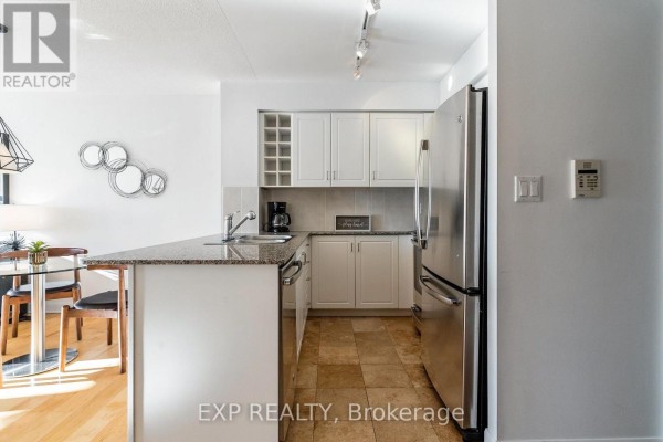 Kitchen with stainless steel refrigerator, white cabinets, granite countertops, and tile flooring. - 3205 - 210 Victoria Street, Toronto