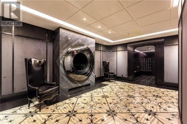 Hallway with two black leather chairs, mirrored circular art, and a mail room. - 3205 - 88 Blue Jays Way, Toronto