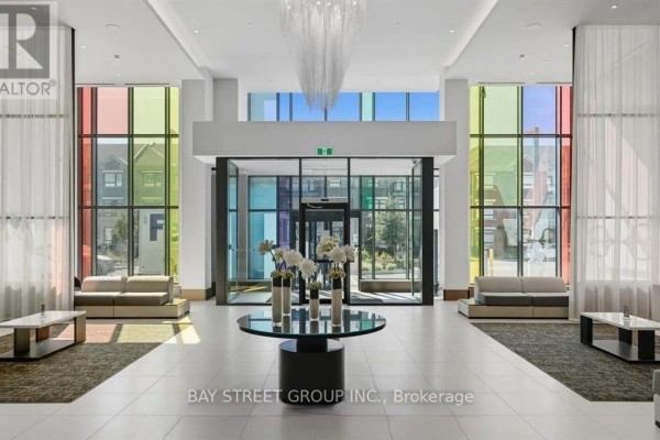 The spacious lobby with floor-to-ceiling windows displaying colorful panels, leading to automatic glass doors and modern seating. - 3207 - 38 Gandhi Lane, Markham
