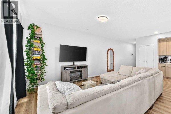 Living room with L-shaped sofa, glass coffee table, fireplace, and television. - 3208, 220 Seton Grove Se, Calgary