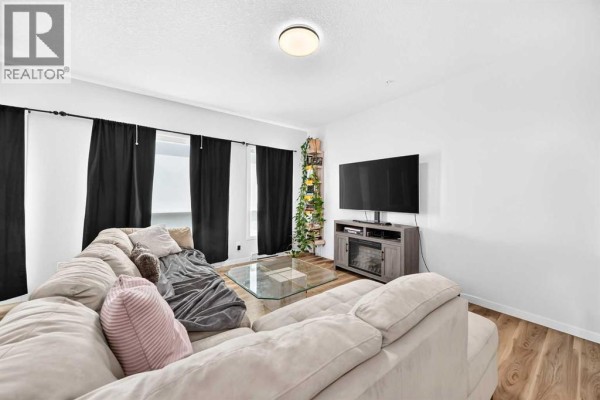 Living room with L-shaped sofa, glass coffee table, black curtains covering windows, and television stand. - 3208, 220 Seton Grove Se, Calgary