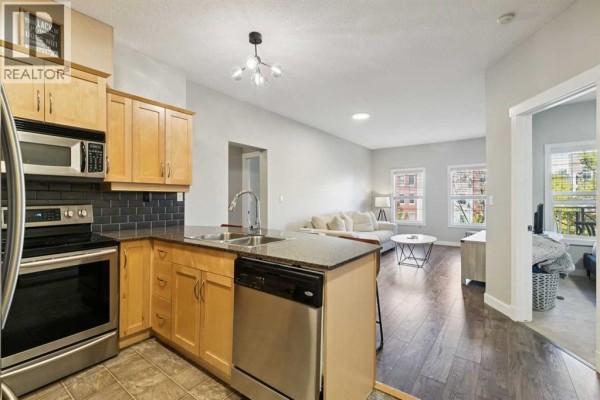 Kitchen with light wood cabinets, granite countertops, stainless steel appliances, and view into living room. - 3209, 5605 Henwood Street Sw, Calgary