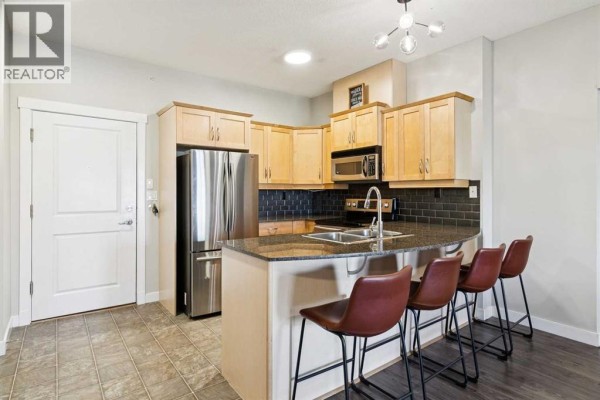 Kitchen with light wood cabinets, granite countertops, stainless steel appliances, and a breakfast bar with four stools. - 3209, 5605 Henwood Street Sw, Calgary