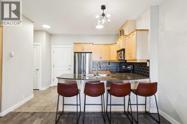 Kitchen with light wood cabinets, granite countertops, stainless steel appliances, and a breakfast bar with four stools. - 3209, 5605 Henwood Street Sw, Calgary