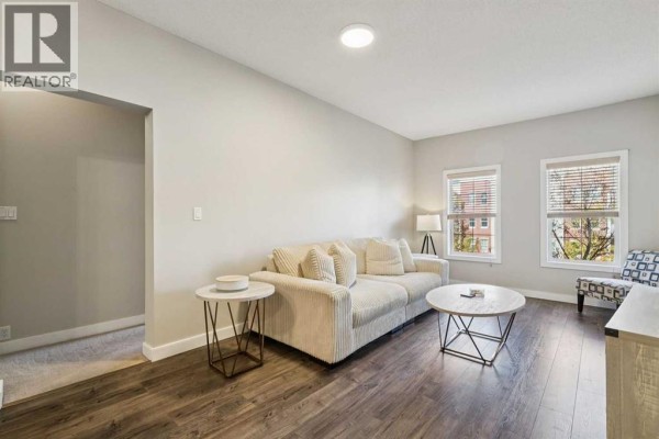 Living room with a cream sofa, two round coffee tables, and a chair, with windows overlooking the street. - 3209, 5605 Henwood Street Sw, Calgary