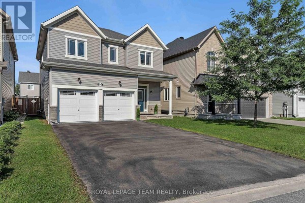 Side exterior view of a two-story house with gray siding and a black asphalt driveway. - 3209 Harvester Crescent, North Grenville