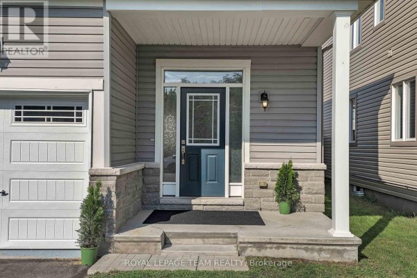 Front entrance porch with gray stone pillars, a blue door, and two small potted evergreens. - 3209 Harvester Crescent, North Grenville