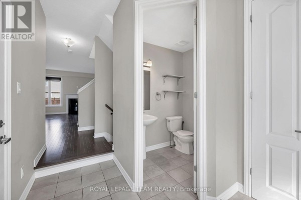 Hallway view showing a powder room with a toilet and sink, and an open doorway to the living area. - 3209 Harvester Crescent, North Grenville