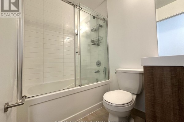 Bathroom with white tiled shower walls, bathtub, toilet, and wooden vanity. - 321 - 621 Sheppard Avenue E, Toronto