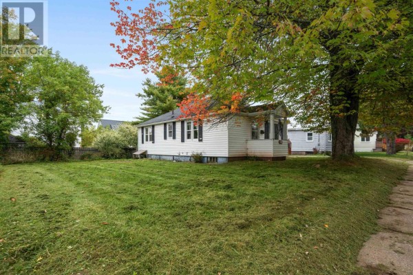 Side view of a white bungalow-style house with a mowed lawn and trees. - 321 Brunswick Street, Truro