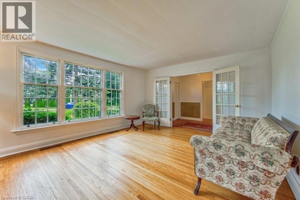 Living room with hardwood floors, large windows, a sofa, and french doors leading to a hallway. - 321 Highland Park, Cambridge