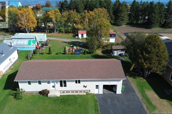Aerial view of bungalow with attached garage, green lawn, and distant ocean view. - 321 Route 134, Petit Rocher Nord