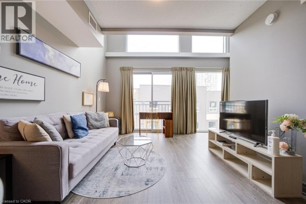 Living room with sofa, coffee table, and television, featuring high ceilings and large windows. - 321 Spruce Street Unit# 710, Waterloo