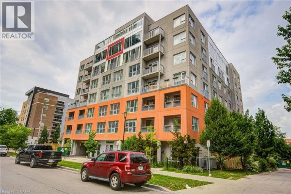 Exterior of a modern apartment building with orange and grey siding, balconies, and parked cars. - 321 Spruce Street Unit# 710, Waterloo