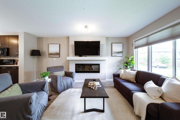 Living room with fireplace, dark sofa, grey armchairs, and large window. - 3211 Cherry Cr Sw, Edmonton