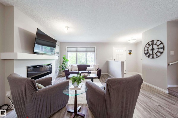 Living room with fireplace, television, grey chairs, and a large window view. - 3211 Cherry Cr Sw, Edmonton