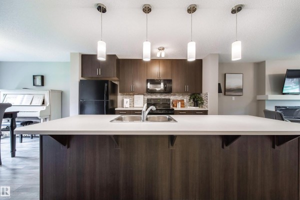 Kitchen island with sink, dark cabinets, and dark brown upper cabinets. - 3211 Cherry Cr Sw, Edmonton