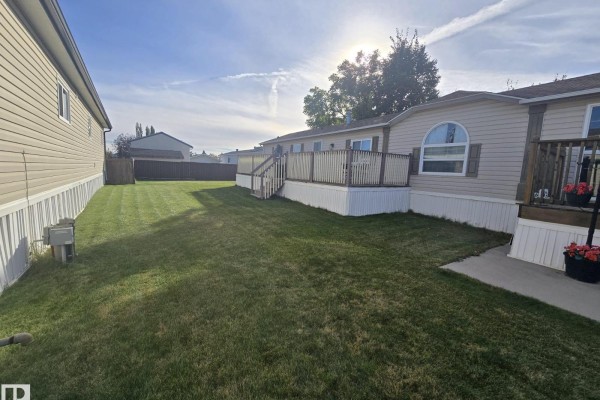 Side view of a mobile home with a large green lawn and a wooden deck. - 3213 Lakewood Close Nw Nw, Edmonton