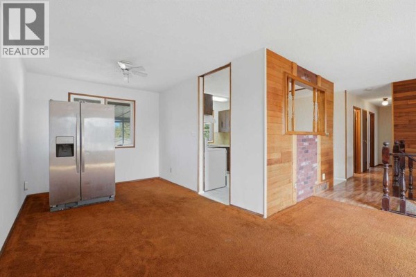 Room with stainless steel refrigerator, window, and opening to kitchen and staircase. - 3214 57 Avenue, Red Deer