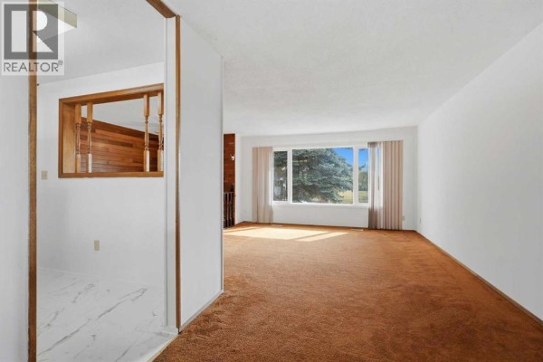 View of living room with large window, brown carpet, and wood accent wall. - 3214 57 Avenue, Red Deer