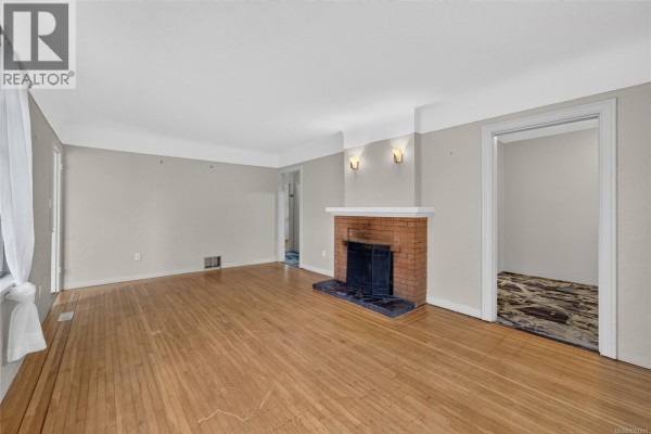 Living room with hardwood floors, a brick fireplace, and doorway to another room. - 3219 Rutledge St, Saanich