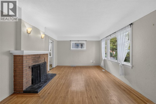 Living room showcasing hardwood floors, a brick fireplace, and white curtains on windows. - 3219 Rutledge St, Saanich