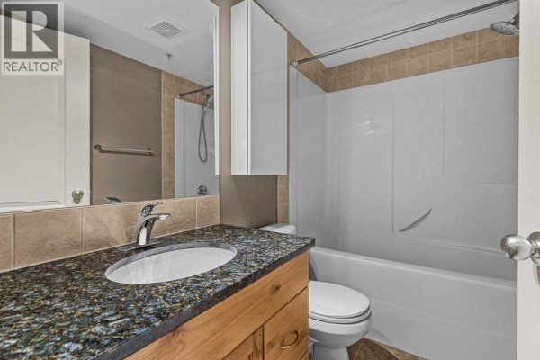 Bathroom vanity with a granite countertop, sink, and wooden cabinets. - 322, 300 Palliser Lane, Canmore