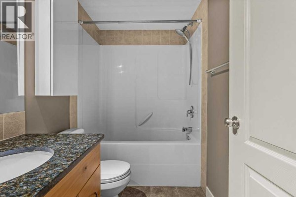 View of a bathtub, toilet, and vanity in a bathroom with tiled walls. - 322, 300 Palliser Lane, Canmore