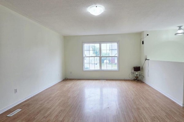 Empty living room with light wood laminate flooring, white walls, and a large window overlooking the street. - 322 Fleming Drive, London East