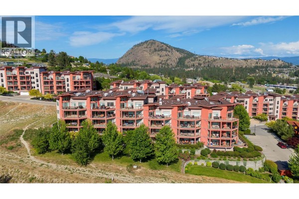 Aerial view of apartment buildings with balconies and surrounding green trees. - 3220 Skyview Lane Unit# 302, West Kelowna