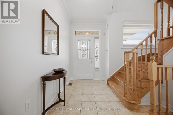 Tiled foyer with a white front door, glass sidelights, a console table, and wooden stairs. - 3225 Escada Drive, Mississauga