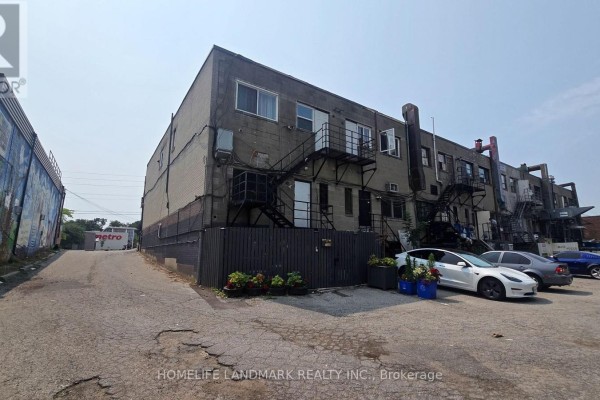 Rear exterior of commercial building with grey brick, metal stairs, and parking. - 3226 Eglinton Avenue E, Toronto