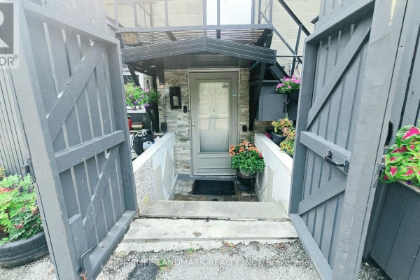 Exterior entrance with grey wooden gates, stone facade, and potted plants. - 3226 Eglinton Avenue E, Toronto