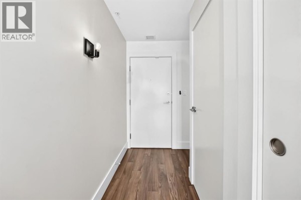Long interior hallway with white doors and dark sconce lighting on the right wall. - 323, 510 Edmonton Trail Ne, Calgary
