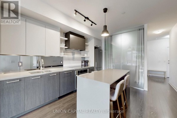 Open concept kitchen and living area with grey and white cabinetry and large windows. - 323 - 1830 Bloor Street W, Toronto
