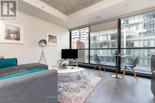 Living area with grey sectional sofa, white coffee table, and view through large windows. - 323 - 629 King Street W, Toronto