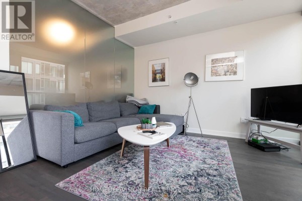 Living room with sectional sofa, floor lamp, and mirrored wall reflecting city buildings. - 323 - 629 King Street W, Toronto