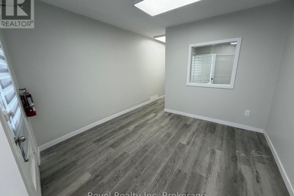 Interior space with light gray walls, gray wood-look flooring, a small window, and a fire extinguisher. - 323 Algonquin Avenue, North Bay