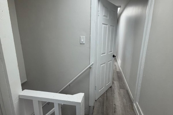 Interior hallway with light gray walls, gray wood-look flooring, and a white door opening into a narrow passage. - 323 Algonquin Avenue, North Bay